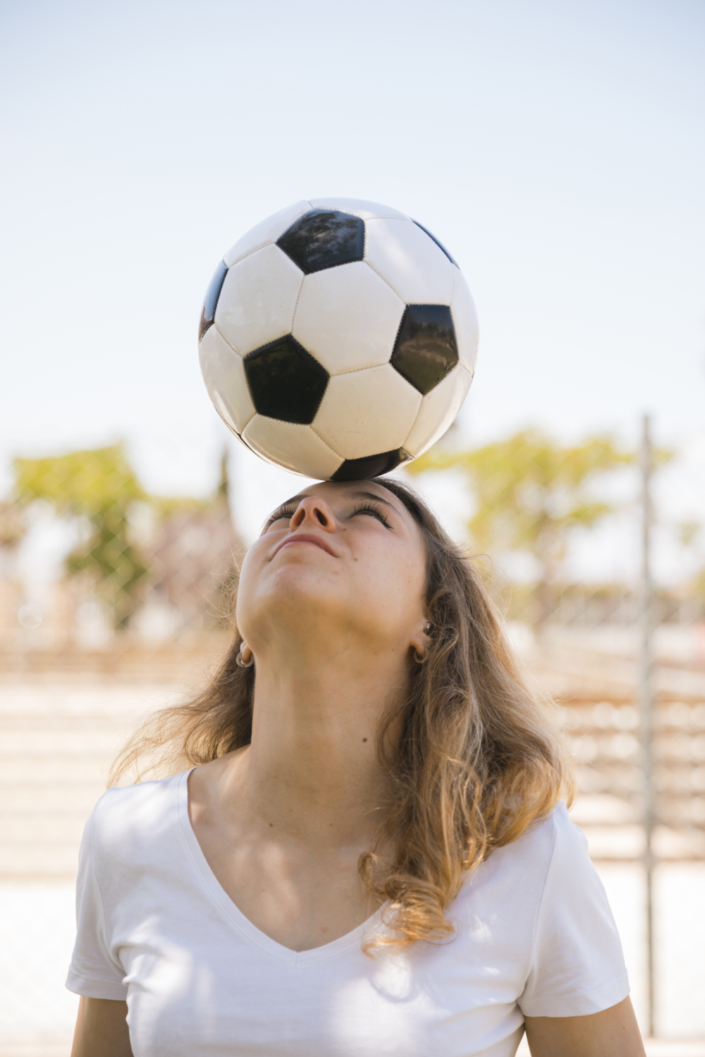 young blonde female balancing soccer ball head in stadium